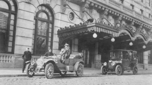 Historic black-and-white photo of vintage cars parked outside an ornate building with decorative architecture.