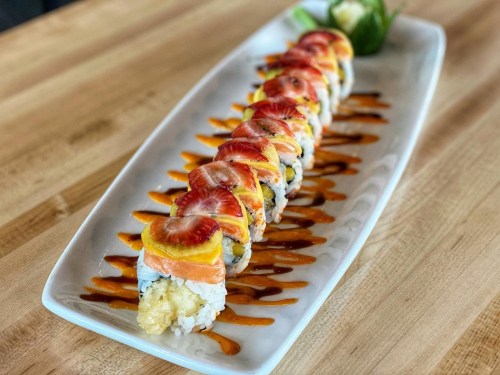 A platter of sushi rolls topped with slices of fruit and drizzled with sauce, presented on a white plate.