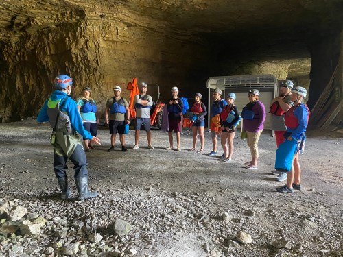 A group of people in helmets and life jackets listens to an instructor in a cave-like setting.