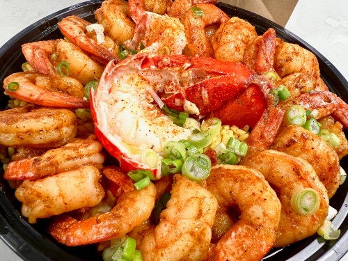 A large platter of shrimp and lobster, garnished with green onions and spices, served over a bed of corn.