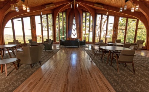 A spacious, wooden interior with large windows, tables, and chairs, offering a scenic view of nature outside.