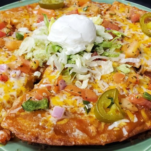 A delicious pizza topped with cheese, tomatoes, lettuce, jalapeños, and a dollop of sour cream on a green plate.