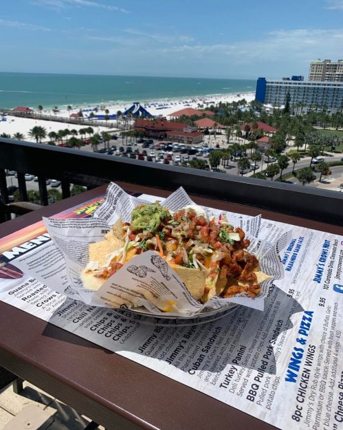 A plate of nachos topped with guacamole and bacon, overlooking a beach and ocean view.