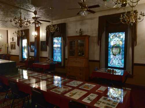 A vintage room with stained glass windows, chandeliers, and a long table set with various items and displays.