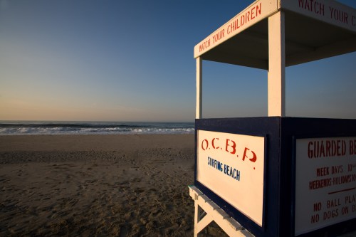 Lifeguard tower on a beach at sunset, with waves in the background and a sign warning to watch children.