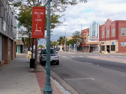 A quiet street in Lamar, featuring storefronts, a welcome banner, and cloudy skies.