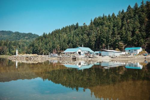 A serene lakeside scene with a forested backdrop, featuring buildings and a lighthouse reflected in calm water.