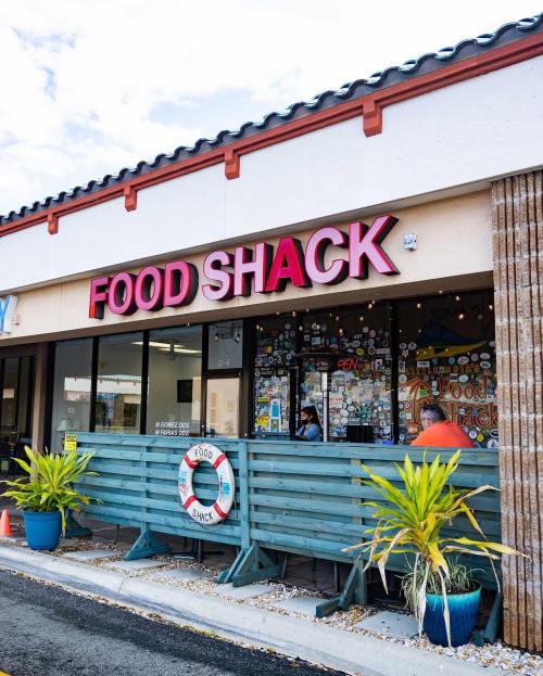 Exterior of a restaurant called "Food Shack," featuring colorful signage and a patio with plants and decor.