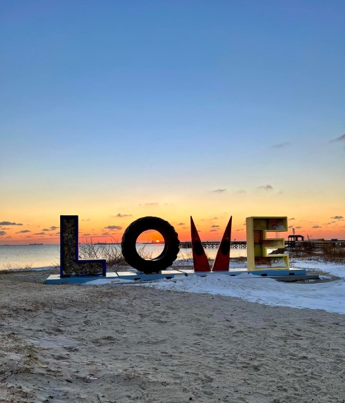 Colorful "LOVE" sign on a beach at sunset, with a serene sky and water in the background.