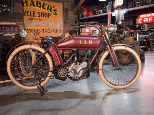 A vintage red motorcycle with a unique design, displayed in a rustic bike shop setting.