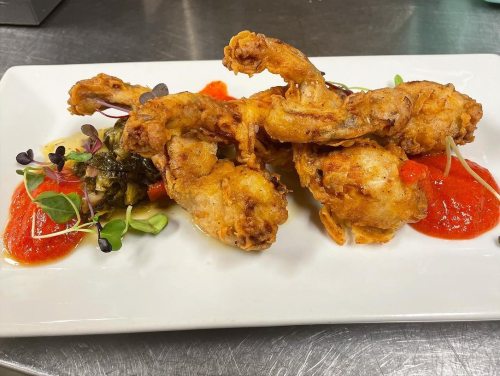 Crispy fried chicken wings on a plate, garnished with sauces and fresh herbs.
