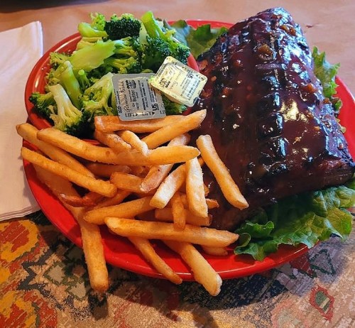 A red plate with BBQ ribs, French fries, and steamed broccoli, garnished with lettuce and a small sauce packet.