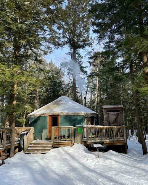 A cozy yurt in a snowy forest, with smoke rising from the chimney and surrounded by tall trees.