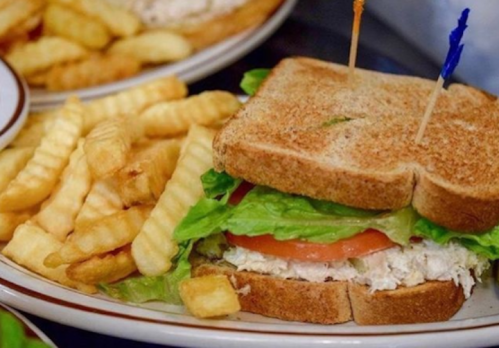 A toasted sandwich with lettuce, tomato, and chicken, served with a side of crinkle-cut fries.
