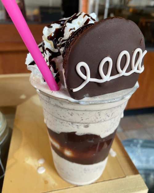 A delicious milkshake topped with whipped cream, chocolate syrup, and a chocolate cookie.