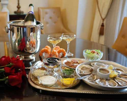 A luxurious dining setup with oysters, shrimp, caviar, champagne, and roses on a table.