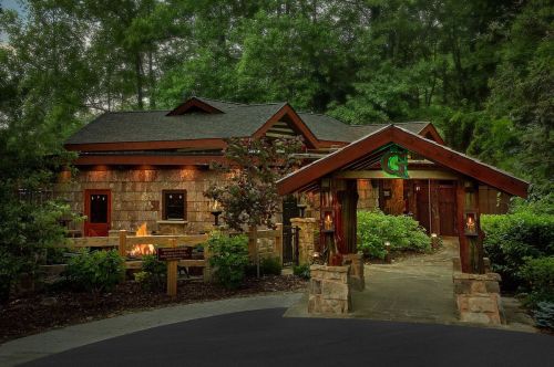 A cozy stone cabin surrounded by greenery, featuring a wooden entrance and warm lighting.