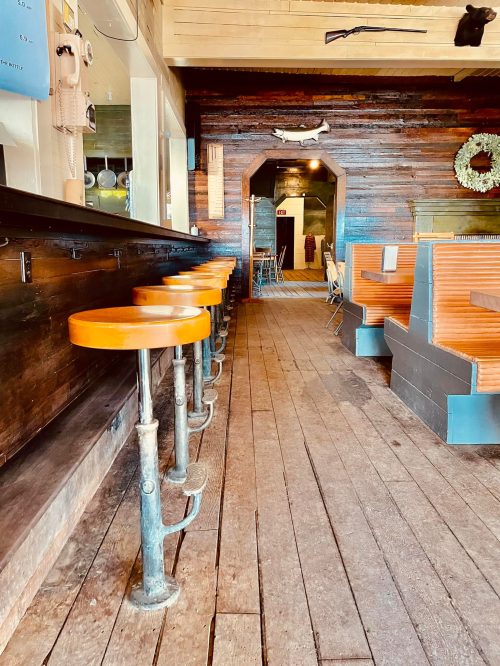 Interior of a rustic bar with orange stools, wooden floors, and a cozy atmosphere.
