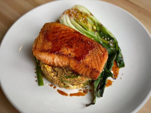 A plate featuring a grilled salmon fillet on a bed of quinoa and vegetables, garnished with sesame seeds.