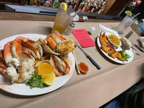 Two plates of seafood on a bar counter: one with crab legs and the other with fried shrimp and sides. Drinks in the background.