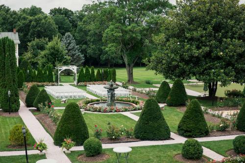 A landscaped garden featuring neatly trimmed hedges, a fountain, and rows of white chairs set for an outdoor event.