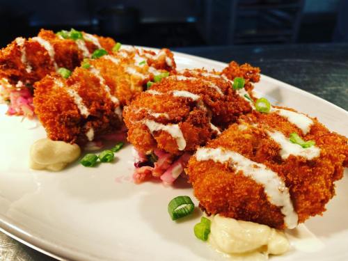 Three crispy fried chicken pieces on a plate, garnished with green onions and drizzled with sauce, served on a bed of slaw.