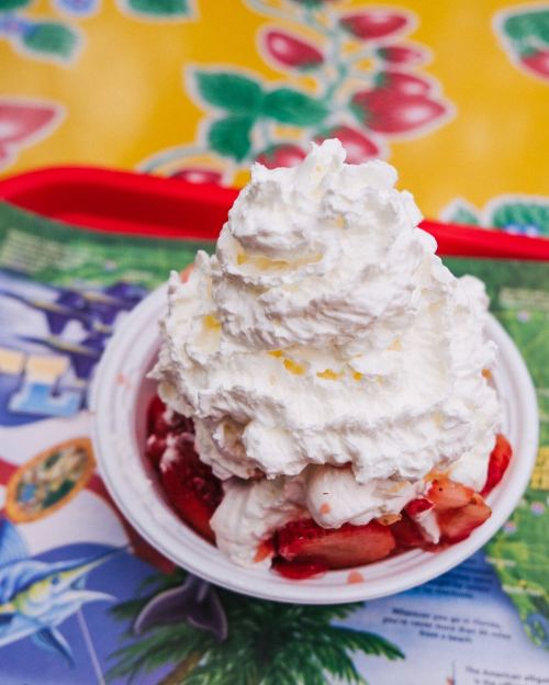 A bowl of dessert topped with whipped cream and strawberries, set on a colorful table.