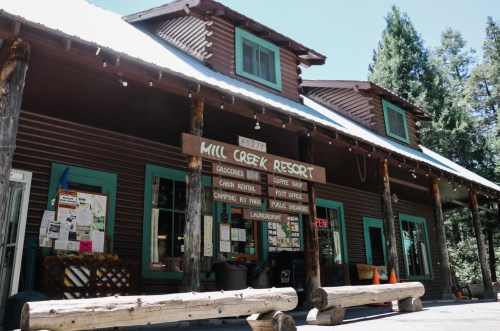 A rustic lodge with green windows and a wooden sign displaying services like groceries, coffee, and camping.
