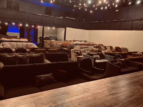 A cozy venue with multiple couches arranged for seating, dimly lit with string lights overhead.