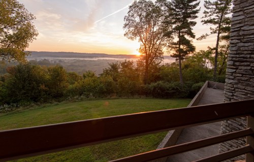 A serene sunrise over a misty landscape, viewed from a balcony surrounded by trees.