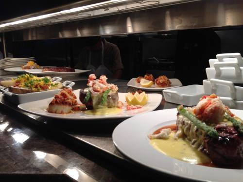 A variety of gourmet dishes displayed, including seafood and steak, under warm kitchen lighting.