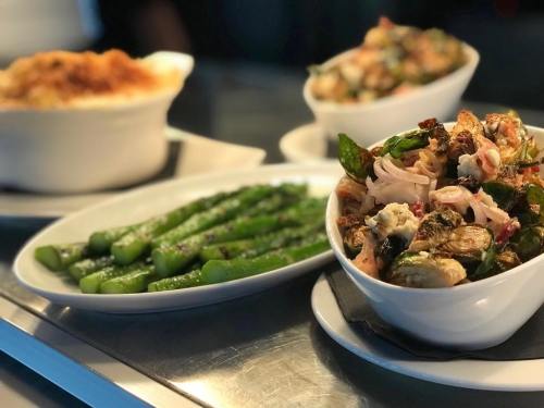 A variety of dishes including asparagus, a mixed vegetable salad, and a creamy baked dish in the background.