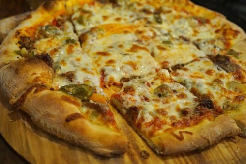 A close-up of a freshly baked pizza with melted cheese, toppings, and a golden crust, partially sliced on a wooden board.