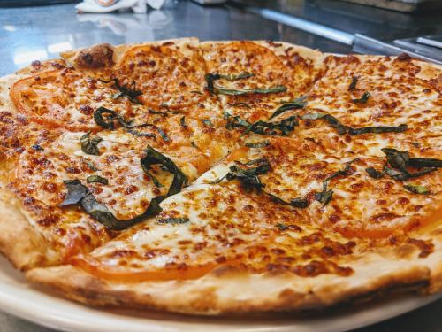 A freshly baked pizza with melted cheese, tomato slices, and basil leaves on a wooden surface.