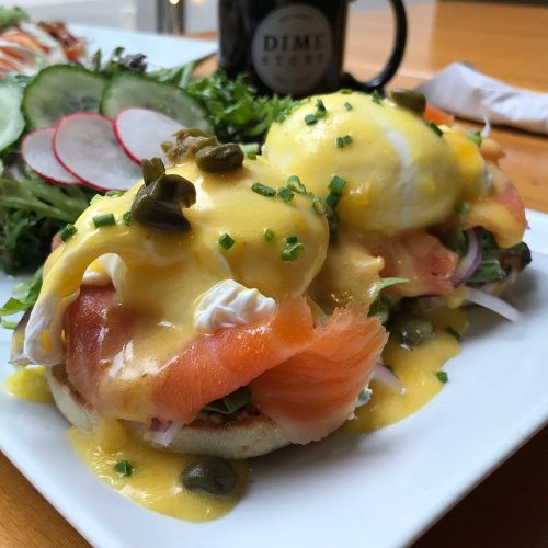 A plate of eggs Benedict with smoked salmon, hollandaise sauce, and a side salad featuring radishes and greens.