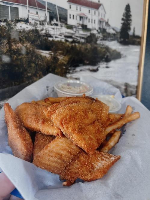 A plate of golden fried fish fillets served with fries and dipping sauces, set against a scenic background.