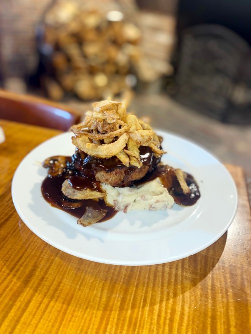 A plate of meatloaf topped with crispy onions, served with mashed potatoes and a rich brown sauce.