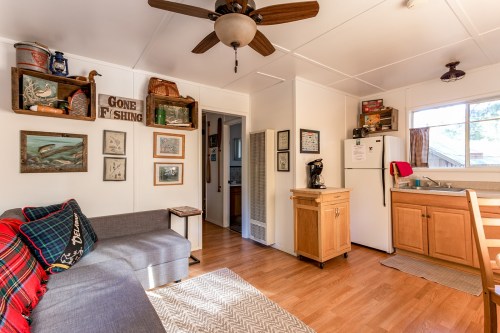 Cozy interior of a small cabin with a kitchen, living area, and fishing-themed decor. Bright and inviting atmosphere.