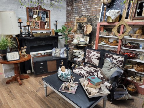 A cozy vintage shop display featuring a cow-print sofa, rustic decor, and various antiques on shelves and tables.