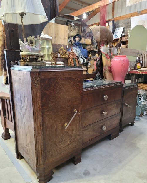 A vintage wooden dresser with a marble top, featuring drawers and decorative details, in an antique shop setting.