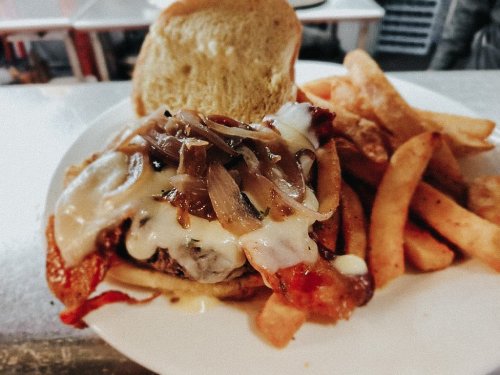 A juicy burger topped with melted cheese, grilled onions, and bacon, served with crispy fries on the side.