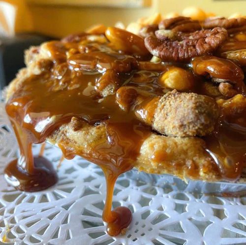 Close-up of a caramel-drizzled pie topped with nuts, resting on a decorative lace doily.
