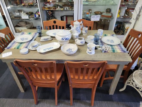 A rustic wooden table set with blue and white dishware, surrounded by four wooden chairs in a vintage shop.