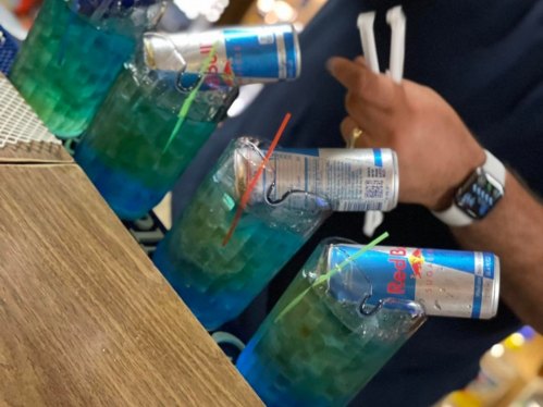 Colorful cocktails with Red Bull cans, garnished with straws, on a wooden bar surface.