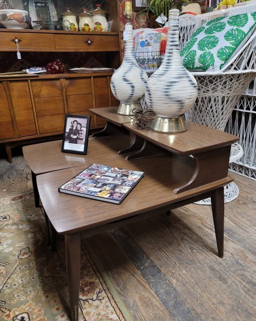 A wooden coffee table with two decorative lamps, a framed photo, and a magazine on top, set in a vintage decor environment.