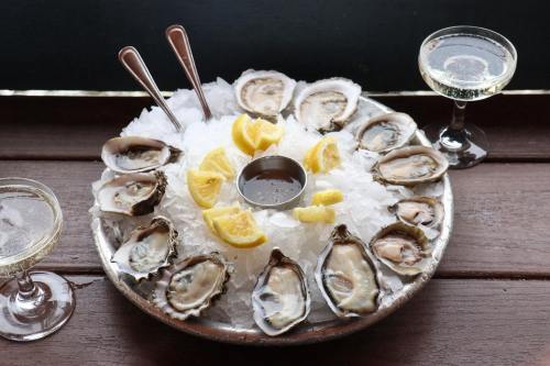 A platter of fresh oysters on ice, garnished with lemon wedges, accompanied by two glasses of sparkling wine.
