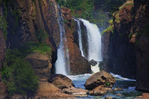 A scenic waterfall cascading over rocky cliffs into a serene pool below, surrounded by lush greenery.