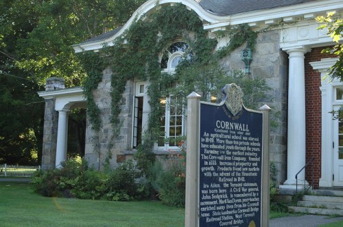 Historic building with ivy-covered stone facade and a sign reading "CORNWALL," surrounded by trees and greenery.