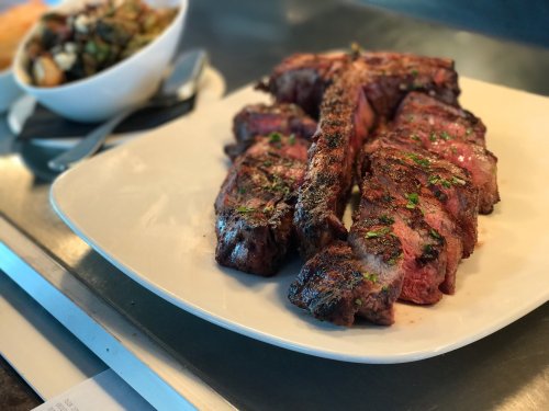 A platter of grilled steak slices garnished with herbs, alongside a bowl of mixed vegetables.