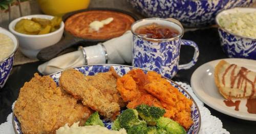 A plate of fried chicken, sweet potatoes, broccoli, and sides, with a cup of tea and cornbread in the background.